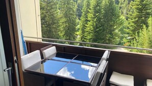 Een balkon met een glazen tafel en rieten stoelen, met uitzicht op een bos.