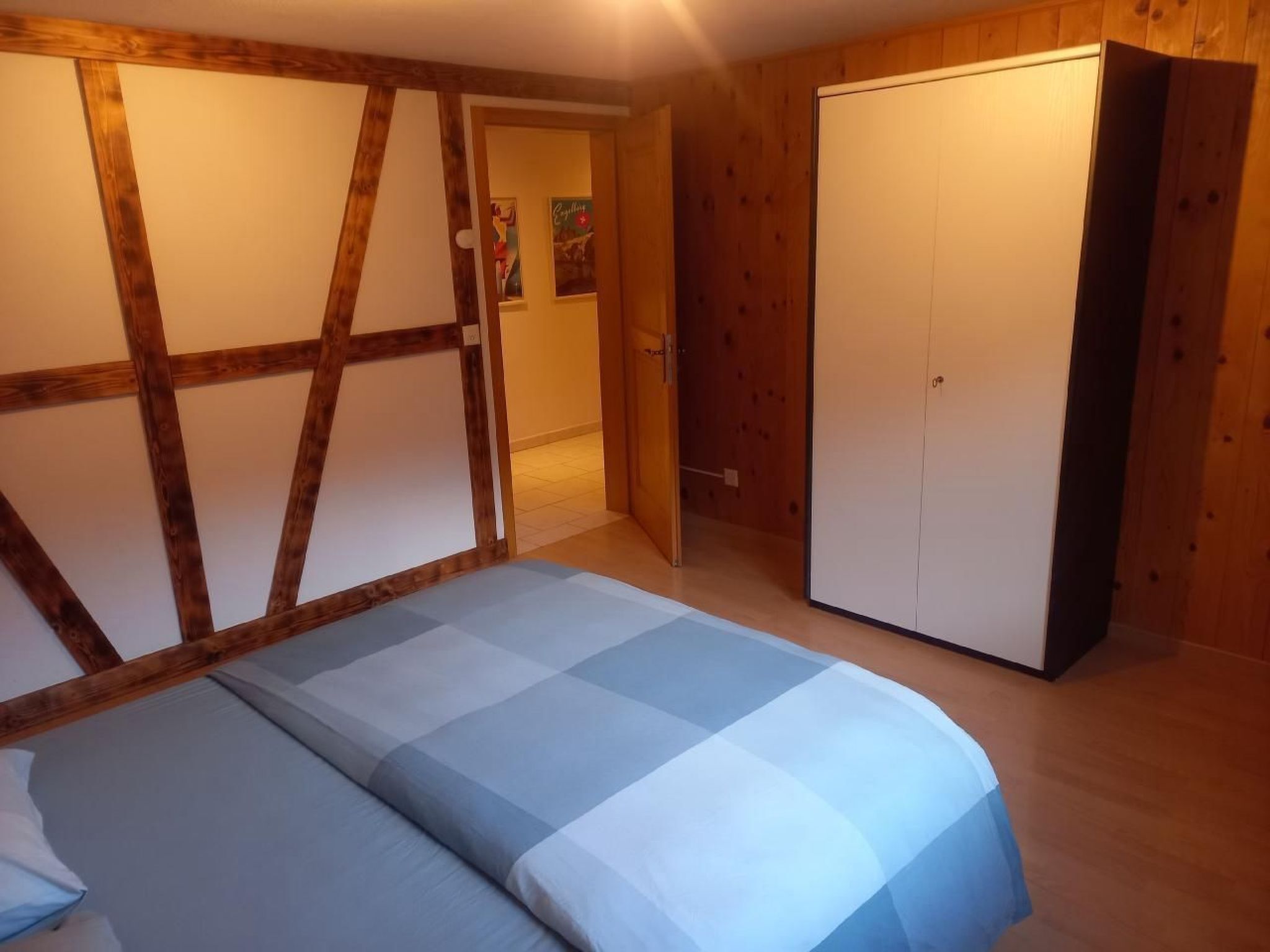 A bedroom with a bed, wooden walls, a wardrobe, and a door leading to another room.