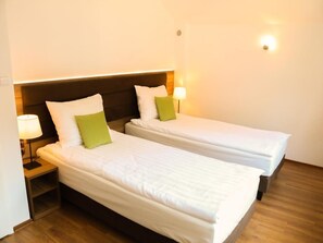 Ein Hotelzimmer mit zwei Einzelbetten, jeweils mit Kissen und einer Nachttischlampe.