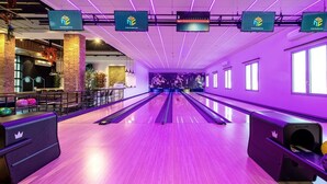 Une salle de bowling avec plusieurs pistes, un bar doté de tabourets et un plafond illuminé par des néons.
