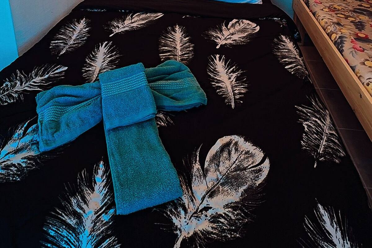 A single bed with a black bedspread featuring white feather patterns, a wooden headboard, and a single hanging light fixture above it.