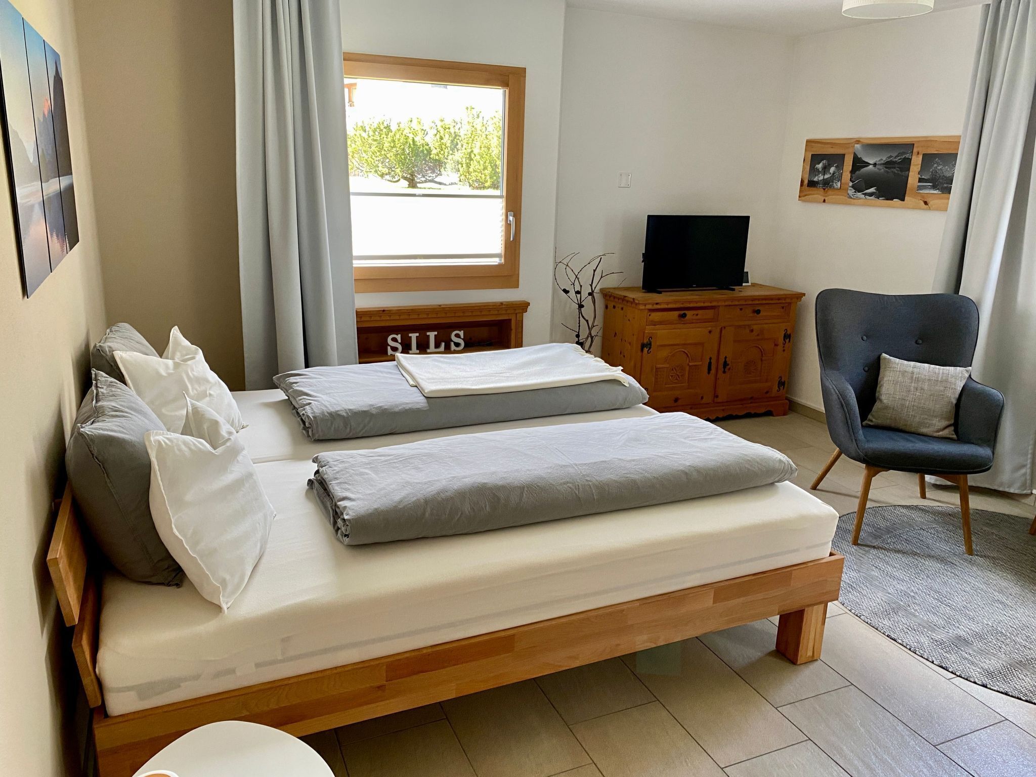 Une chambre à coucher avec un lit, une télévision, une chaise et une fenêtre avec des rideaux.
