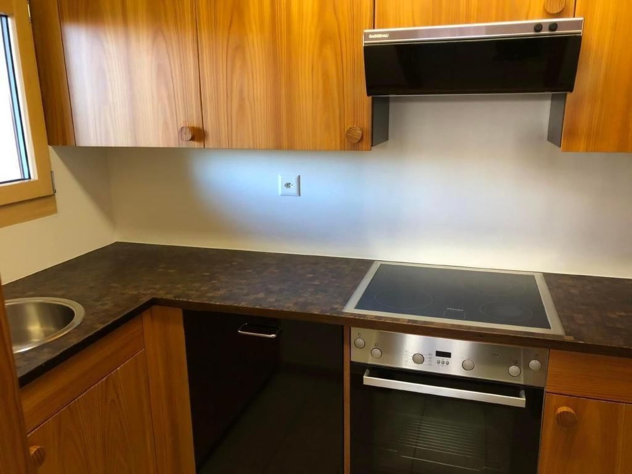 Une cuisine dotée de meubles en bois, d’un évier en acier inoxydable, d’un four encastré et d’une plaque de cuisson à induction.