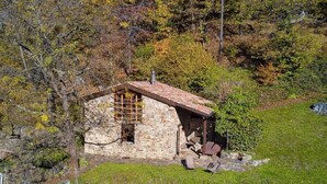 Un pequeño edificio de piedra con techo inclinado, ventana de madera y un banco en el exterior.