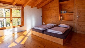 Un dormitorio de cabaña de madera con dos camas, una ventana con vistas a árboles y una estantería.