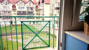 Un balcón con una reja metálica verde, vista a una zona residencial con edificios de varios pisos y un pequeño jardín.