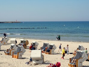 A beach with rows of striped beach chairs and umbrellas, a pier in the background, and people walking along the shore. - Appartement in Nowe Miasto mit Garten by Interhome (Kolobrzeg)
