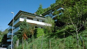 A multi-story building with balconies, surrounded by greenery and a clear sky. - Al Bosco 71A by Interhome (Lugano)