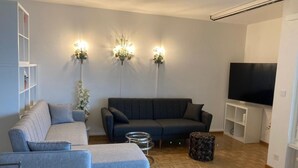 Ein modernes Wohnzimmer mit einem grauen Sofa, einem blauen Sofa, einem Fernseher und drei Wandleuchten.