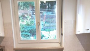 Eine kleine Küche mit Fenster, weißen Schränken, einer Holz Arbeitsplatte, einer Heizung und einem Geschirrspüler.