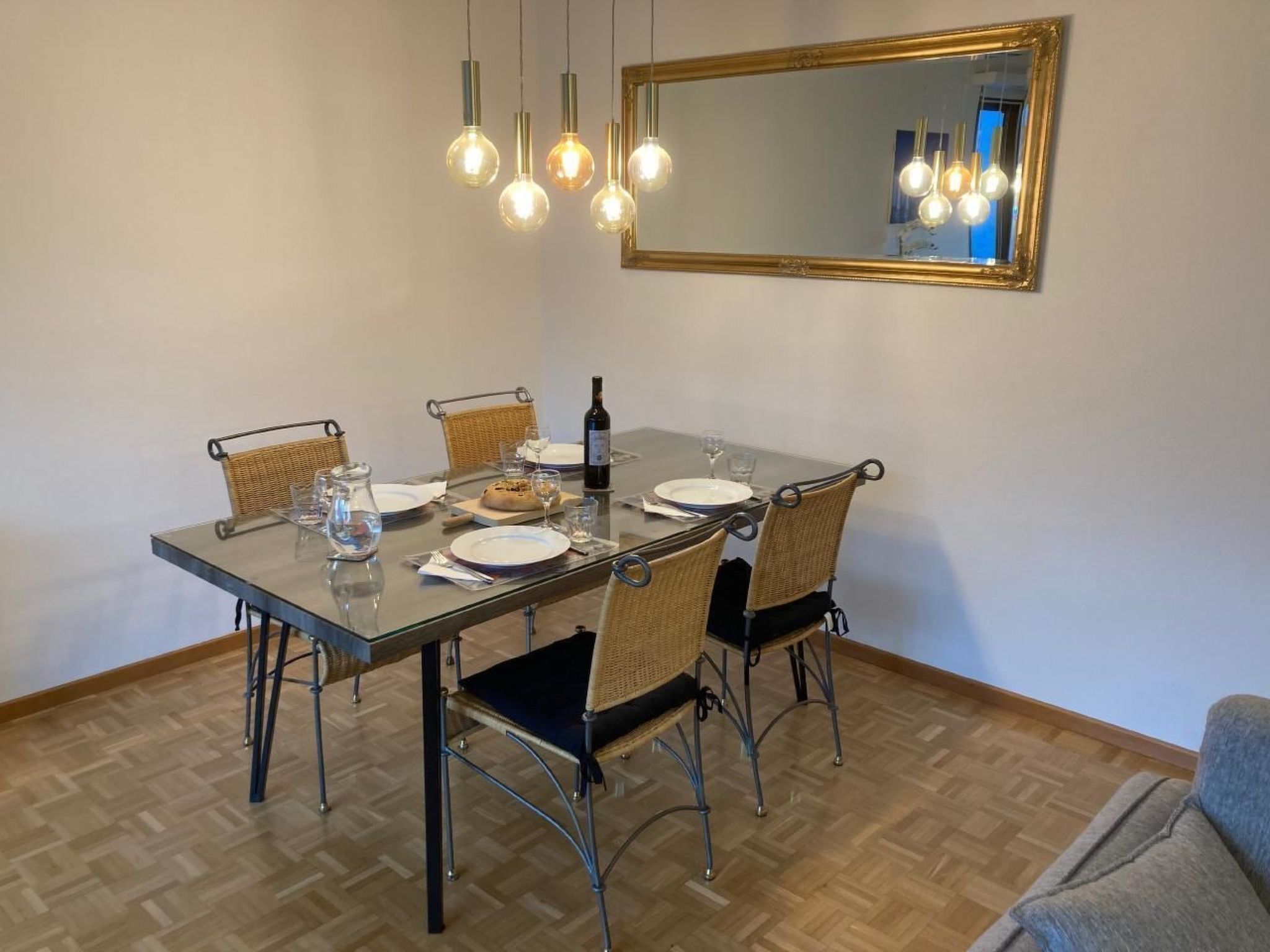 Un coin repas avec une table en verre, des chaises en osier et un miroir au-dessus.