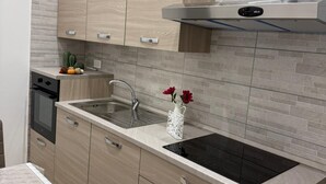 Una cocina moderna con armarios de madera clara, una campana extractora de acero inoxidable, una placa de cocina por inducción negra y un lavamanos.