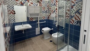 Baño con ducha, inodoro y lavamanos, con azulejos estampados y cabina de ducha de cristal.