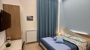 Un dormitorio moderno con cama, escritorio, silla, televisor y radiador.