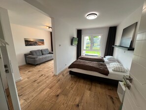 Un dormitorio con cama, televisor, ventana con vistas y una sala de estar independiente con sofá.