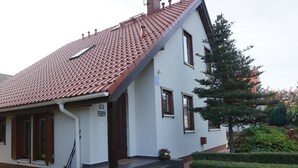 Een woonhuis met twee verdiepingen, een rode dakbedekking, een voortuin met treden en een klein tuintje.