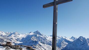 Une croix en bois, dressée au sommet d’une montagne, avec en arrière-plan des pics enneigés.