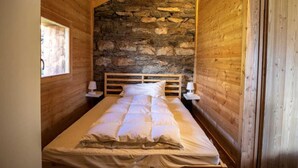Une chambre confortable avec un mur en pierre, des poutres apparentes en bois au plafond, un lit avec une literie blanche et deux lampes de chevet.
