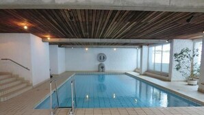 Une piscine intérieure dotée d’un sol carrelé, d’un plafond en bois et d’un escalier menant à un niveau supérieur.