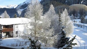 Un paysage montagneux enneigé avec un bâtiment doté d’un toit en pente et d’une terrasse en bois.