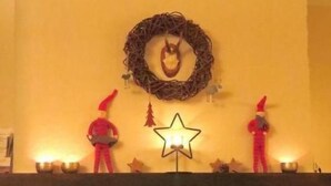 Une cheminée surmontée d’un luminaire en forme d’étoile, de part et d’autre duquel se trouvent deux figurines du Père Noël, toutes deux de couleur rouge.