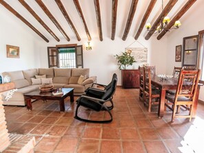 A living room with a sofa, a coffee table, a dining table with chairs, a chandelier, and a window with blinds. - Casa vacanze Casa de Cantoblanco by Interhome (Los Romanes)