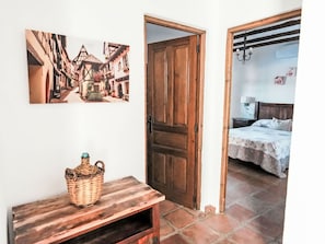 Quarto com porta de madeira, cama com colcha florida e quadro pendurado na parede retratando uma cena de rua.