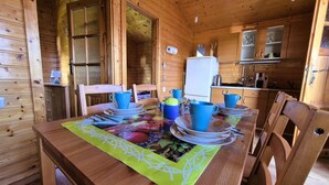 Ein Holzblockhaus-Interieur mit einem Esstisch, gedeckt für vier Personen, mit blauen Tassen und Tellern, und einem Kühlschrank im Hintergrund.