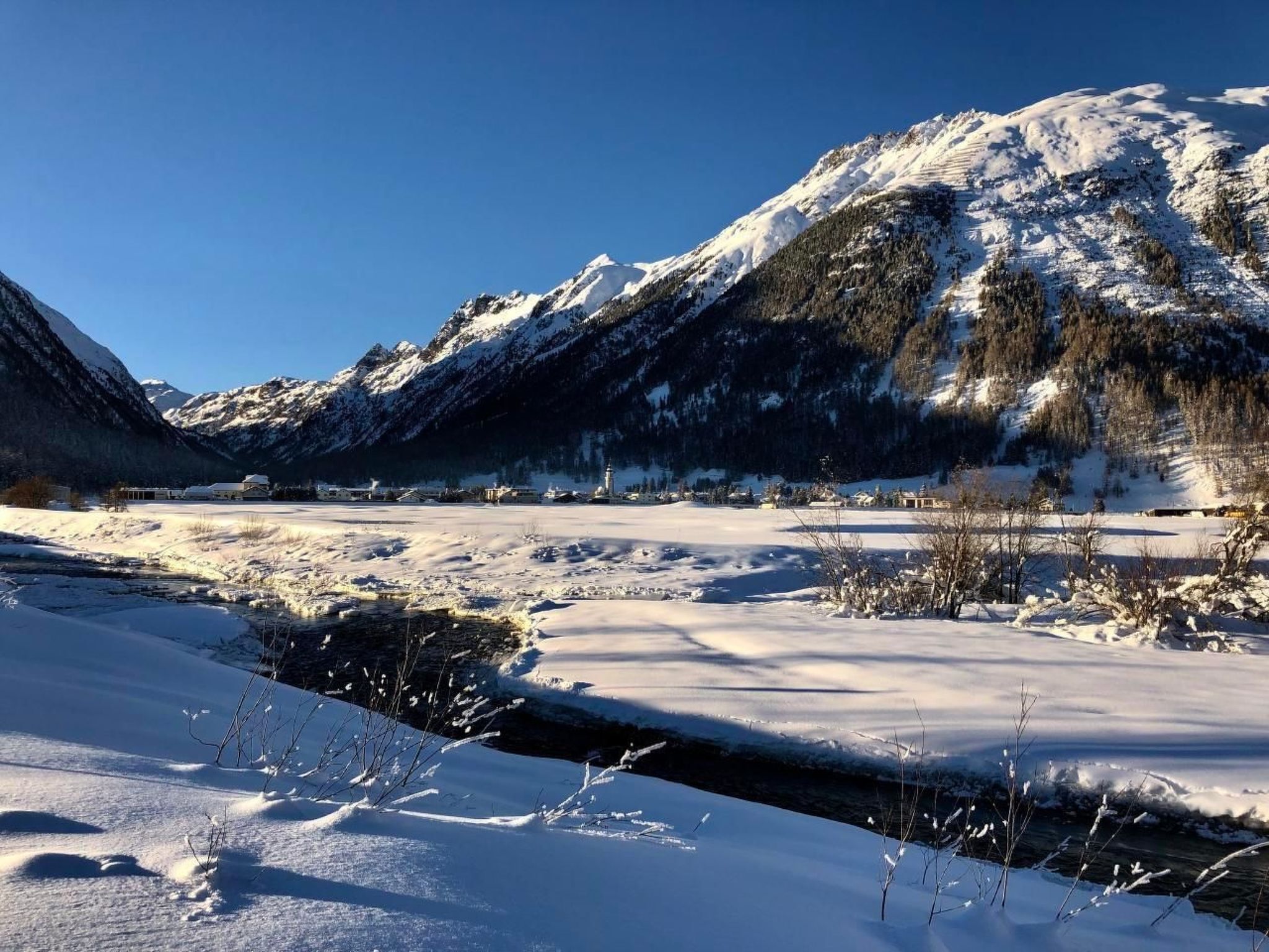 A snow-covered landscape with mountains, a river, and a small settlement.
