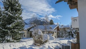 Paisatge cobert de neu amb una muntanya al fons, una tanca de fusta i un edifici amb el teulat ple de neu.