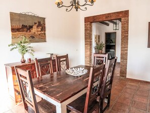 Ein Essbereich mit Holztisch und -stühlen, einer Chandelüster, einem Gemälde und einer Ziegelwand.