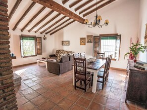 A spacious living area with a high ceiling, exposed wooden beams, a dining table with chairs, a sofa, and a chandelier. - Cantoblanco Häuser 2 by Interhome (Los Romanes)