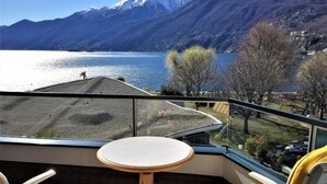 A balcony with a table and striped chairs overlooking a lake and mountains. - Palazzo Ascolago Nr. 27 by Interhome (Ascona)