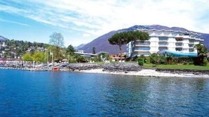 A coastal hotel with a mountain backdrop, a marina, and a clear sky. - Palazzo Ascolago Nr. 27 by Interhome (Ascona)