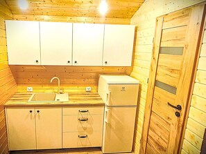 Eine kleine Küche mit Holzwänden, weißen Schränken, einem Spülbecken und einem kleinen Kühlschrank.