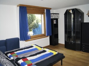 Ein Schlafzimmer mit einem Bett, einem Fenster mit Vorhängen, einem Kleiderschrank und einer kleinen Kommode.