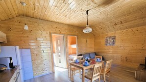 Interior de una cabaña de madera con cocina, comedor y una puerta que da al exterior.