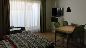 A hotel room with a bed, a TV, a dining table with chairs, and a window with curtains. - Casa Torri by Interhome (St. Moritz)
