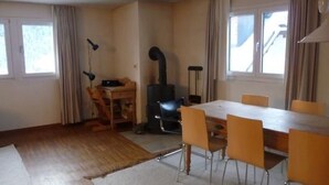 Ein Zimmer mit Holzboden, einem Esstisch mit Stühlen, einem schwarzen Heizkörper und einem Fenster mit Vorhängen.
