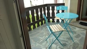Ein Balkon mit einem blauen Tisch, einem Holzstuhl, einem schwarzen Geländer und Blick auf Gebäude im Hintergrund.