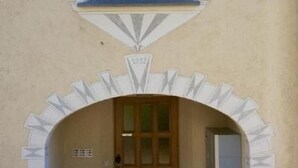 Ein Gebäudeeingang mit einer Holztür, einem kleinen Fenster darüber und einem dekorativen Bogen.