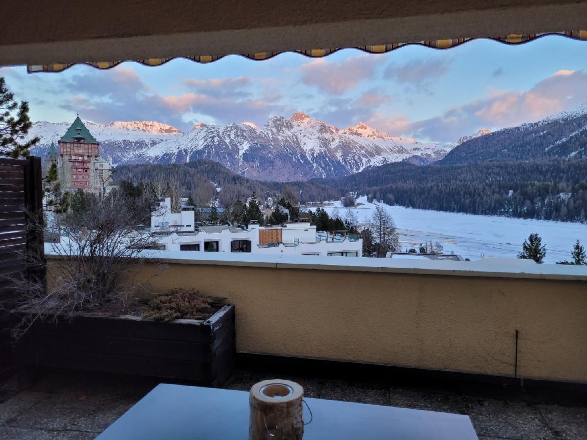 A view from a balcony overlooking a snowy landscape with mountains, a church, and a small town.