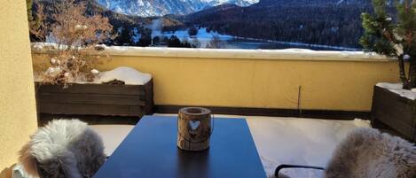 En balkon med et bord og stole, der kigger ud over et sneklædt bjerglandskab.
