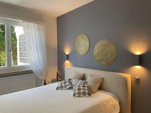 A bedroom with a bed, two wall-mounted lamps, and a window with curtains. - Casa Bijou by Interhome (Locarno)