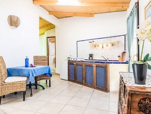 Eine Küche mit blauen Fliesen an der Rückwand, einem Holzespeisetisch mit Korbstühlen und einer Orchidee im Topf auf einem Holznachttisch.