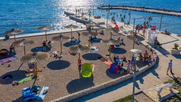 Una playa con sombrillas, tumbonas y una zona de piscina.