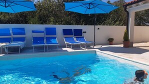 Una piscina con sillas reclinables y sombrillas azules.