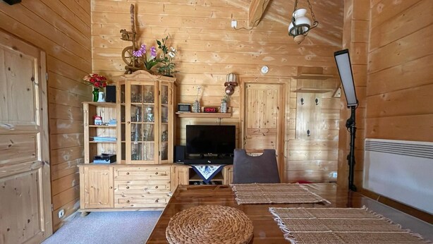 A wooden cabin interior with a dining table, chairs, a television, and a cabinet with glass doors. - Uns Hüsung by Interhome (Rerik)