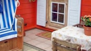 A red building with a wooden door and white shutters, a small table with chairs, and a blue and white striped towel on a chair. - Uns Hüsung by Interhome (Rerik)