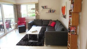 A modern living room with a grey sectional sofa, a red armchair, a coffee table, and a bookshelf. - Exklusives Apartment, am Luganersee, mit Außenpool by Interhome (MAROGGIA)